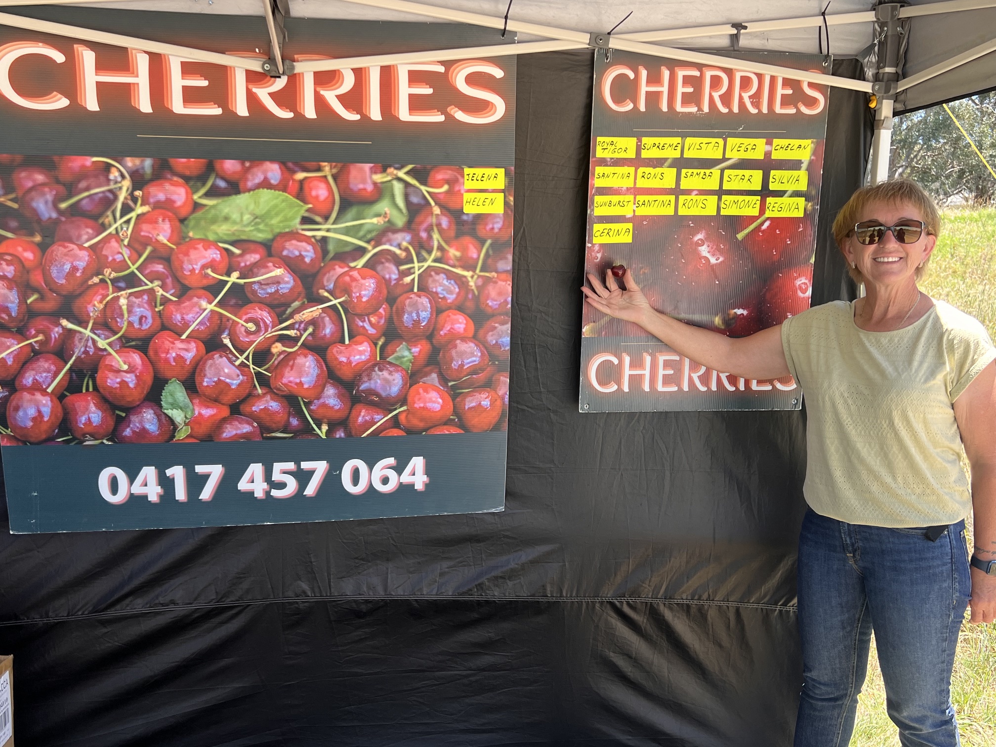 Cerina Cherries owner pointing out the cherry varieties on the stall's signage board
